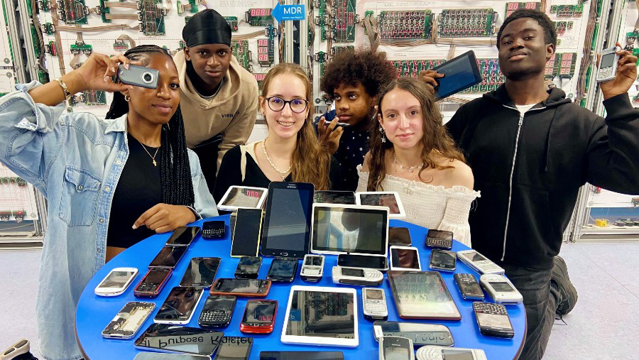 A group fo young people with a range of old phones and tablets on a table